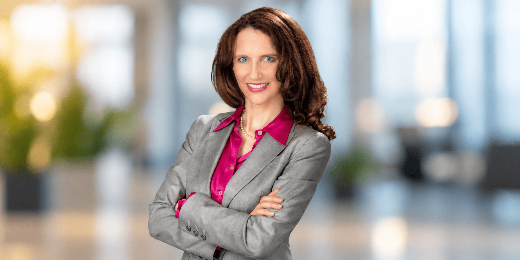 Professional woman in a gray suit and pink blouse standing with arms crossed