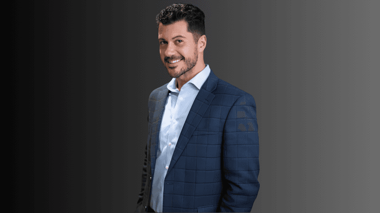 Man in a blue plaid suit smiling against a gradient background